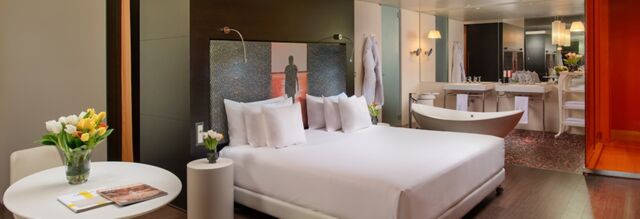Modern hotel room at Nhow Milano featuring a large white bed, tulip flowers, freestanding bathtub, and double sinks with mirrors