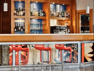 Three red bar stools in front of a modern bar with bottles and glasses on shelves at Holiday Inn Express Milan-Malpensa Airport
