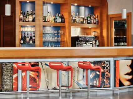Three red bar stools in front of a modern bar with bottles and glasses on shelves at Holiday Inn Express Milan-Malpensa Airport