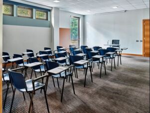 Empty classroom with rows of blue student desks and a teacher's desk in a well-lit room at Holiday Inn Express Milan-Malpensa Airport