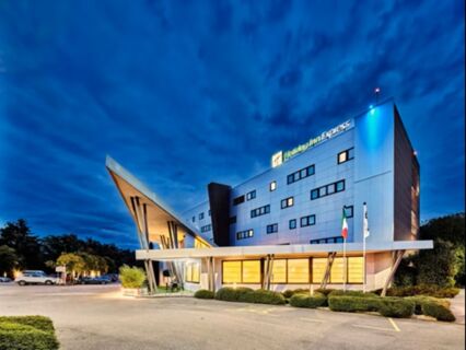 Modern Holiday Inn Express Milan-Malpensa Airport building at dusk with illuminated windows and a sharp angular roof design