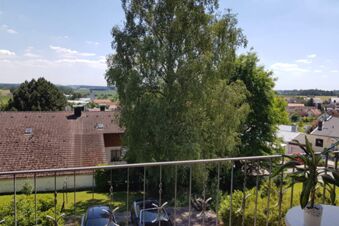 Blick vom Balkon des Hotel Pension Heigl auf gr&uuml;ne B&auml;ume, D&auml;cher von H&auml;usern und eine l&auml;ndliche Umgebung bei Sonnenschein.