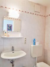 Hell gefliestes Badezimmer mit Waschbecken, Spiegel und WC im Hotel Pension Heigl, dekorativ mit Seife und Lufterfrischer ausgestattet.