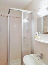 Klares, schlichtes Badezimmer mit Duschkabine, Waschbecken und Spiegel im Hotel Pension Heigl, gepflegte Sanit&auml;ranlagen mit wei&szlig;er Fliesenoptik.