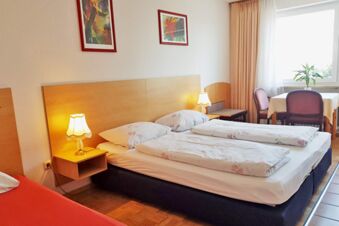 Helles G&auml;stezimmer mit Doppelbett, Leselampen und einem kleinen Tisch am Fenster im Hotel Pension Heigl, gem&uuml;tliche Atmosph&auml;re.