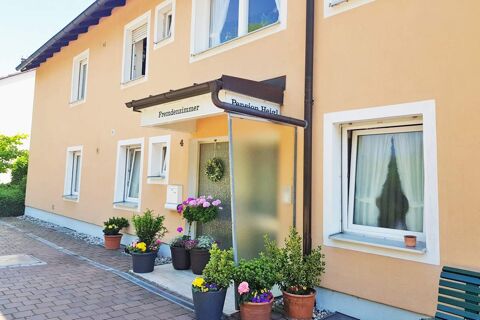 Fassade des freundlichen Hotel Pension Heigl mit gelber Au&szlig;enwand, mehreren Fenstern und bunten Blument&ouml;pfen am Eingang.
