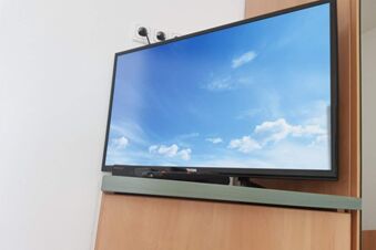 Flacher Fernseher mit Himmelsbild h&auml;ngt an der Wand in einem modernen Zimmer der Hotel Pension Heigl, schlicht eingerichtet.