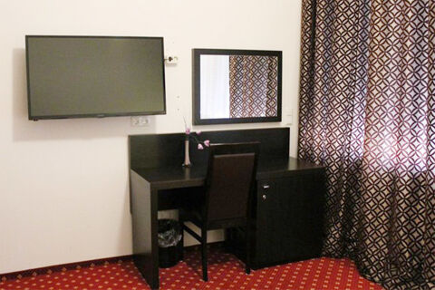 Jednoduch&eacute; pracovn&iacute; m&iacute;sto se stolem, židl&iacute;, zrcadlem a televiz&iacute; v pokoji hotelu Aariana se vzorovan&yacute;mi z&aacute;věsy.