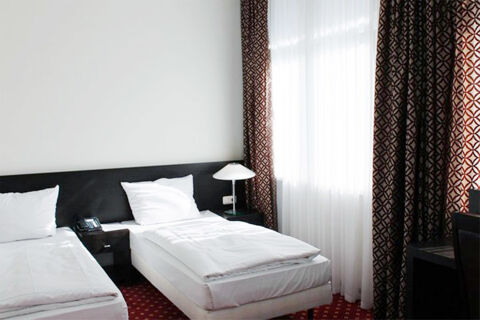 Světle zař&iacute;zen&yacute; pokoj se dvěma samostatn&yacute;mi lůžky a vzorovan&yacute;mi z&aacute;věsy v hotelu Aariana s modern&iacute;m komfortem.
