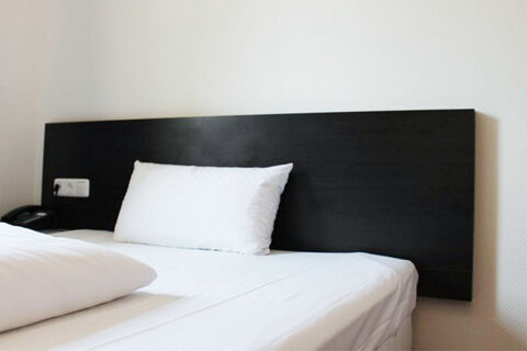 Semplice camera d'albergo con lenzuola bianche e testiera nera dell'Aariana Hotel, progettata in uno stile elegante e moderno.