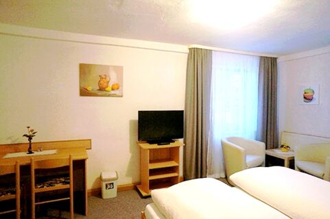 Hotel room at Gasthaus Berger with two beds, a table with chairs, a TV on a wooden stand, and two armchairs by a window