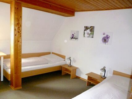 Two single beds with white bedding and wooden frames separated by wooden nightstands with lamps in Gasthaus Berger room