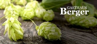 Fresh green hop cones lying on a rustic wooden surface with Gasthaus Berger logo text displayed on the right side