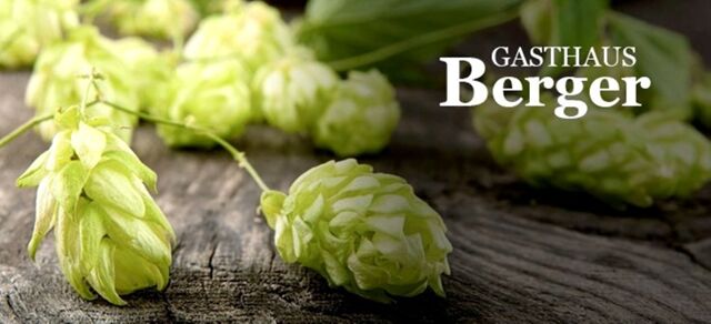 Fresh green hop cones lying on a rustic wooden surface with Gasthaus Berger logo text displayed on the right side