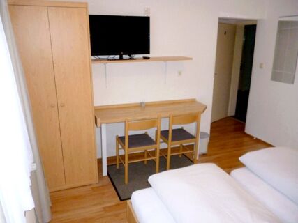 Hotel room at Gasthaus Berger with wooden wardrobe, desk, two chairs, mounted TV, and neatly made bed with white linens