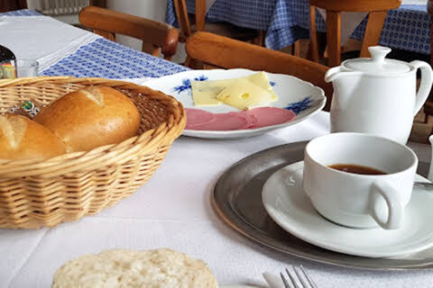 A breakfast setting at Gasthaus Berger with a basket of rolls, sliced cheese, cold cuts, a cup of coffee, and a white teapot on a table