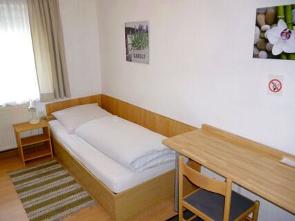 Single wooden bed with white bedding next to a desk and chair in a simple room at Gasthaus Berger