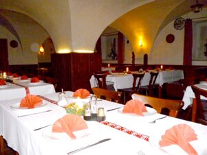 Tables with white tablecloths and pink folded napkins set with cutlery and candles inside the arched dining room of Gasthaus Berger