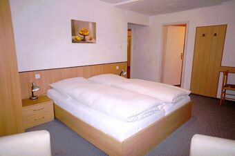 Bedroom at Gasthaus Berger with double bed, bedside tables, lamps, wardrobe, chairs, and a fruit painting on the wall