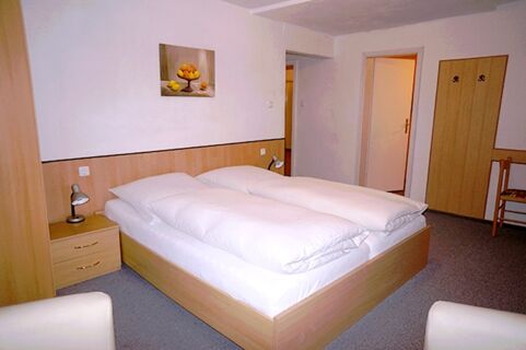 Bedroom at Gasthaus Berger with double bed, bedside tables, lamps, wardrobe, chairs, and a fruit painting on the wall