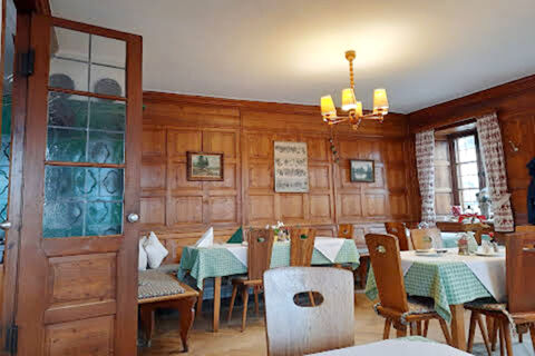 Dining area inside Gasthaus Berger with wooden walls, green checkered tablecloths, and wooden chairs under a chandelier