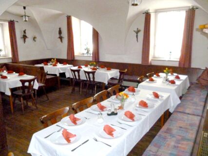 Dining area at Gasthaus Berger with white tablecloths, wooden chairs, folded red napkins, and wall decorations including crucifixes and statues