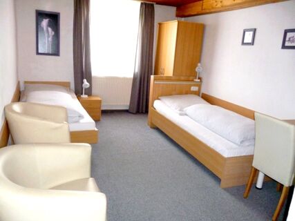 Simple twin bedroom at Gasthaus Berger with two single beds, bedside tables, armchairs, and framed wall art