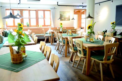 Dining area of Gasthof Br&auml;uwirt with wooden tables and chairs, green table runners, sunflowers, and natural light from windows