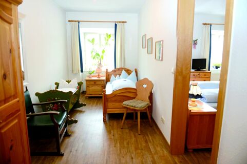 A cozy wooden bedroom with a single bed, nightstand, decorated cradle, chair, and a window at Gasthof Br&auml;uwirt