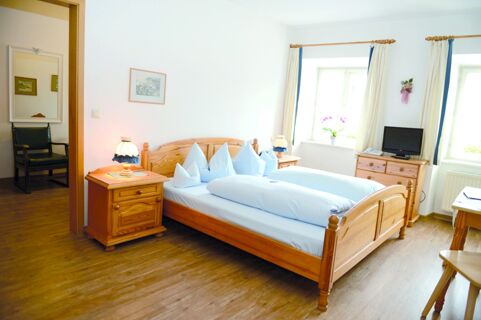 A bright bedroom at Gasthof Br&auml;uwirt with wooden double bed, nightstands, a dresser with TV, and two windows with curtains