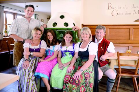Six people sitting and standing indoors wearing traditional Bavarian clothing in Gasthof Br&auml;uwirt restaurant environment