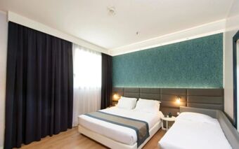 Hotel room at NEO Hotel featuring a double bed and single bed with a padded headboard, teal wallpaper, and a window with curtains