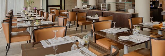 Dining area at NH Hotel Linate with multiple tables set with glassware, plates, cutlery, and brown leather chairs