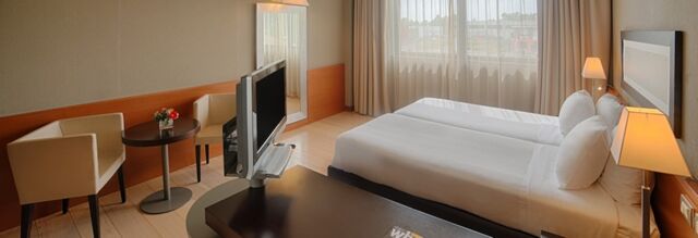Hotel room at NH Hotel Linate featuring two single beds, a TV on a swivel stand, two cream chairs and a small round table with flowers