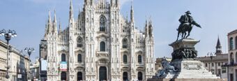 White ornate Gothic cathedral with multiple spires and a large equestrian statue in the foreground near NH Hotel Linate