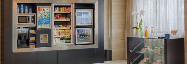 Automated snack and beverage vending area with coffee machine and stocked glass-door refrigerators at NH Hotel Linate lobby