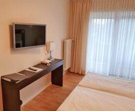 Helles Hotelzimmer im Hotel Frisch mit Doppelbett, Flachbildfernseher an der Wand und einem Schreibtisch mit Telefon und Lampe.