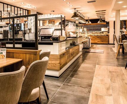 Moderner und gem&uuml;tlicher Fr&uuml;hst&uuml;cksbereich im Hotel Frisch mit Holz- und Fliesenelementen sowie einem Buffet und komfortablen Sitzgelegenheiten.