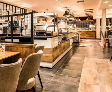 Moderner und gem&uuml;tlicher Fr&uuml;hst&uuml;cksbereich im Hotel Frisch mit Holz- und Fliesenelementen sowie einem Buffet und komfortablen Sitzgelegenheiten.