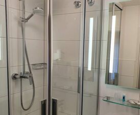 Moderne Badausstattung mit Glasdusche, Spiegel und Beleuchtung im Hotel Frisch zeigt ein sauberes und funktionales Badezimmer.