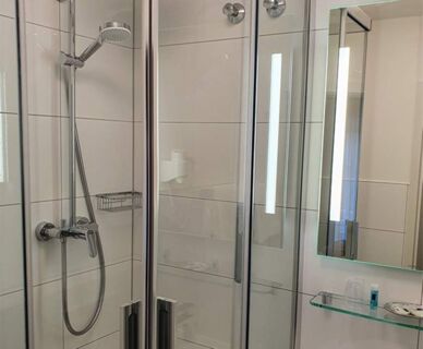 Moderne Badausstattung mit Glasdusche, Spiegel und Beleuchtung im Hotel Frisch zeigt ein sauberes und funktionales Badezimmer.