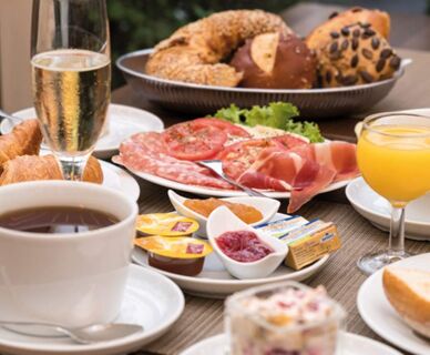 Ein gedeckter Fr&uuml;hst&uuml;ckstisch mit Kaffee, Orangensaft, Geb&auml;ck, Aufschnitt und Marmelade im Hotel Frisch, einladend angerichtet f&uuml;r G&auml;ste.