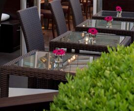 Au&szlig;enbereich mit Glas-Tischen und geflochtenen St&uuml;hlen, dekoriert mit kleinen Vasen und pinken Blumen im Hotel Frisch.