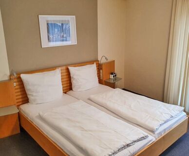 Helles und schlicht eingerichtetes Schlafzimmer mit zwei Einzelbetten im Hotel Frisch, inklusive Nachttischen und dekorativem Bild.