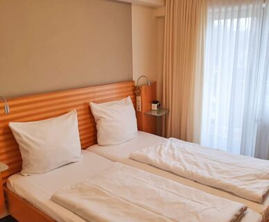 Hell eingerichtetes Doppelzimmer mit zwei Einzelbetten, wei&szlig;en Bettw&auml;sche und gro&szlig;en Fenstern im Hotel Frisch.