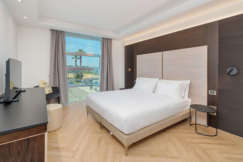 Minimalist guest room at B&B Hotel San Mauro with large bed, wooden floor, TV, and large window with curtains