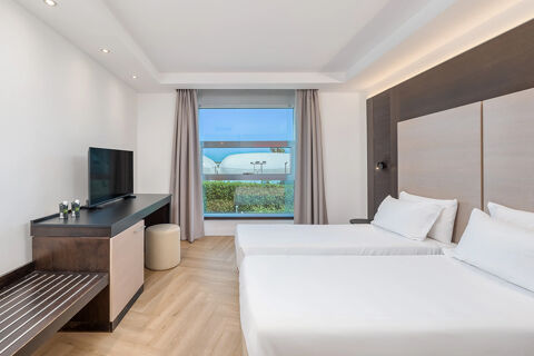 Two single beds with white linens, wooden flooring, TV on a desk, and a window with beige curtains in B&B Hotel San Mauro