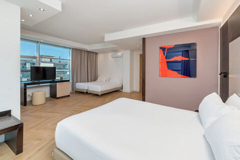 Spacious hotel room at B&B Hotel San Mauro featuring a large bed, two twin beds, TV, desk, and abstract wall art