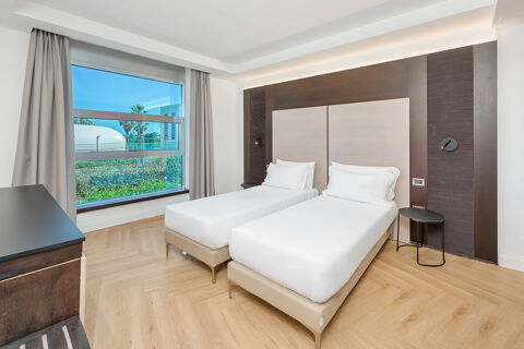 Two single beds with white linens and pillows in a bright room at B&B Hotel San Mauro with a large window and wooden floor
