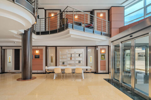 Modern lobby interior of B&B Hotel San Mauro with a white table, wooden chairs, metal railings, and large glass entrance doors
